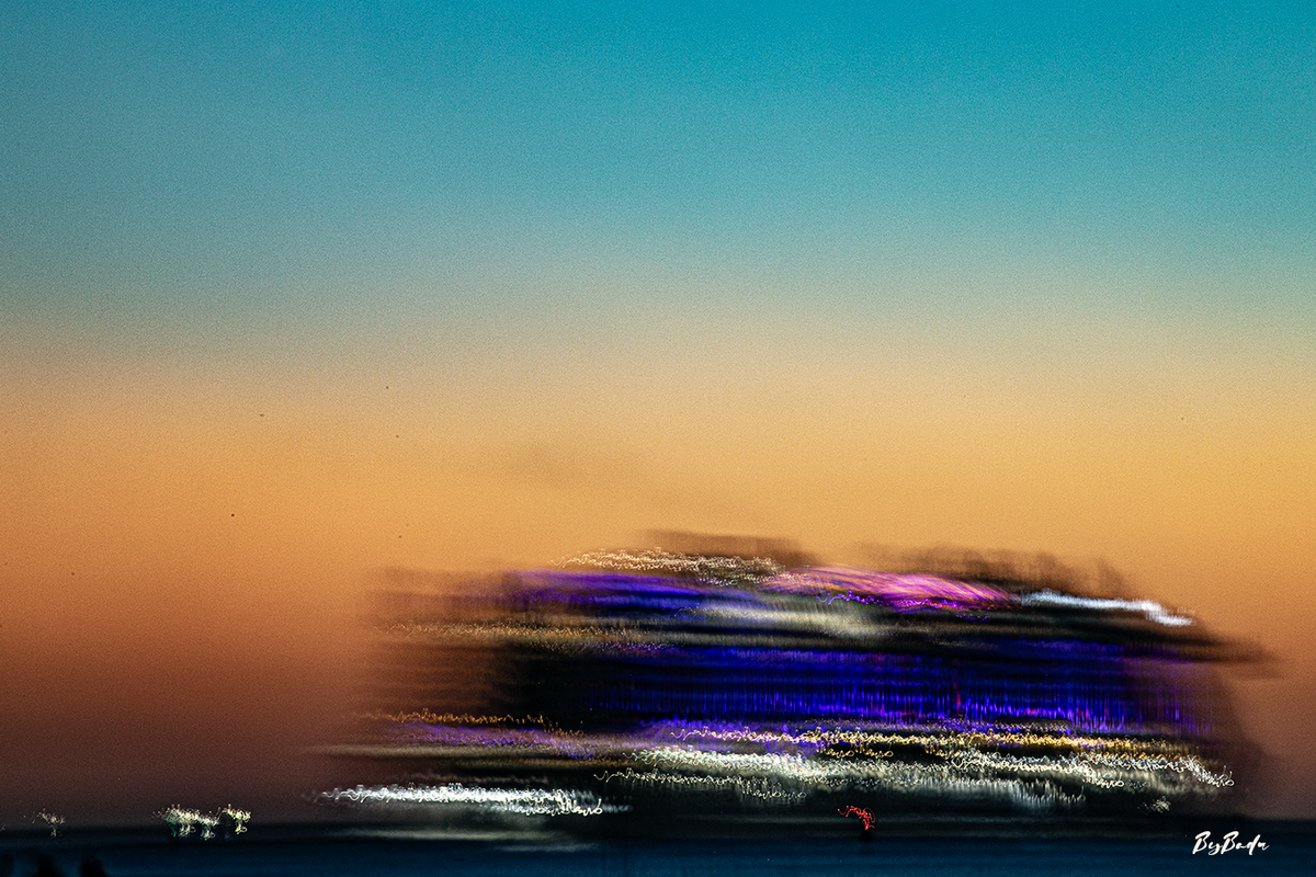 Bateaux de Nuit — navire aux lumières bleues et violettes étirées devant un ciel turquoise et orangé, photographie Bybadr.