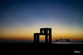 Fenêtre de la nuit — structure géométrique noire devant un ciel doré et bleu, navire illuminé à droite sur la mer | Bybadr
